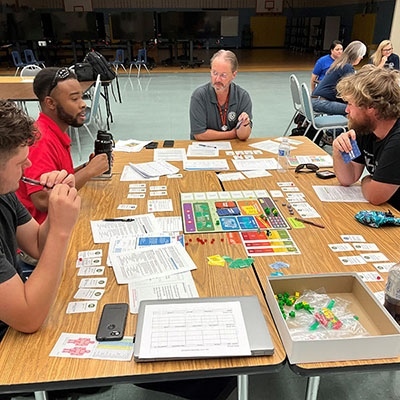 This is a T.E.S.T. participants sit around a table with game materials in front of them.